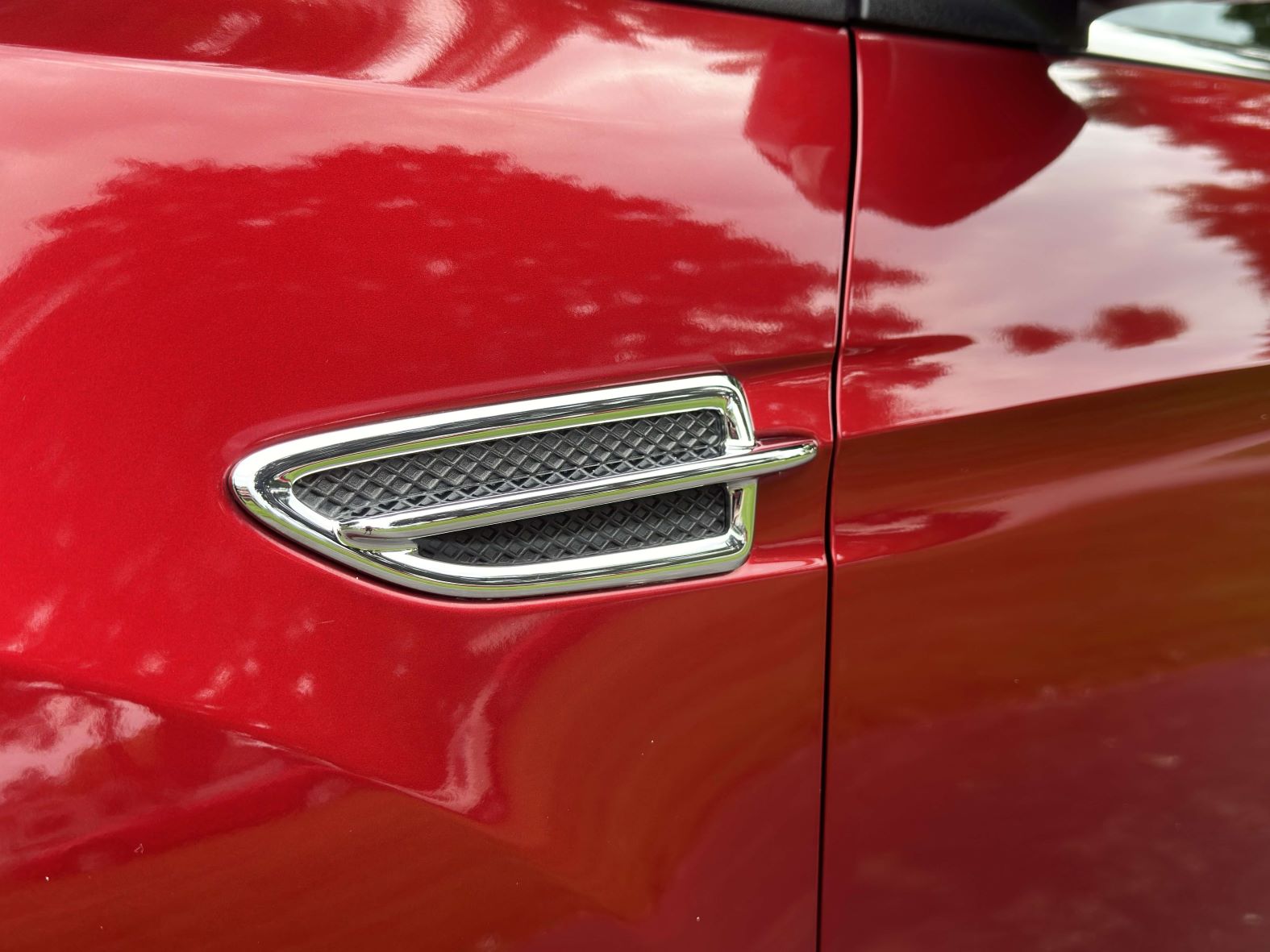 Waxed and polished red car paint around a chrome trim accent